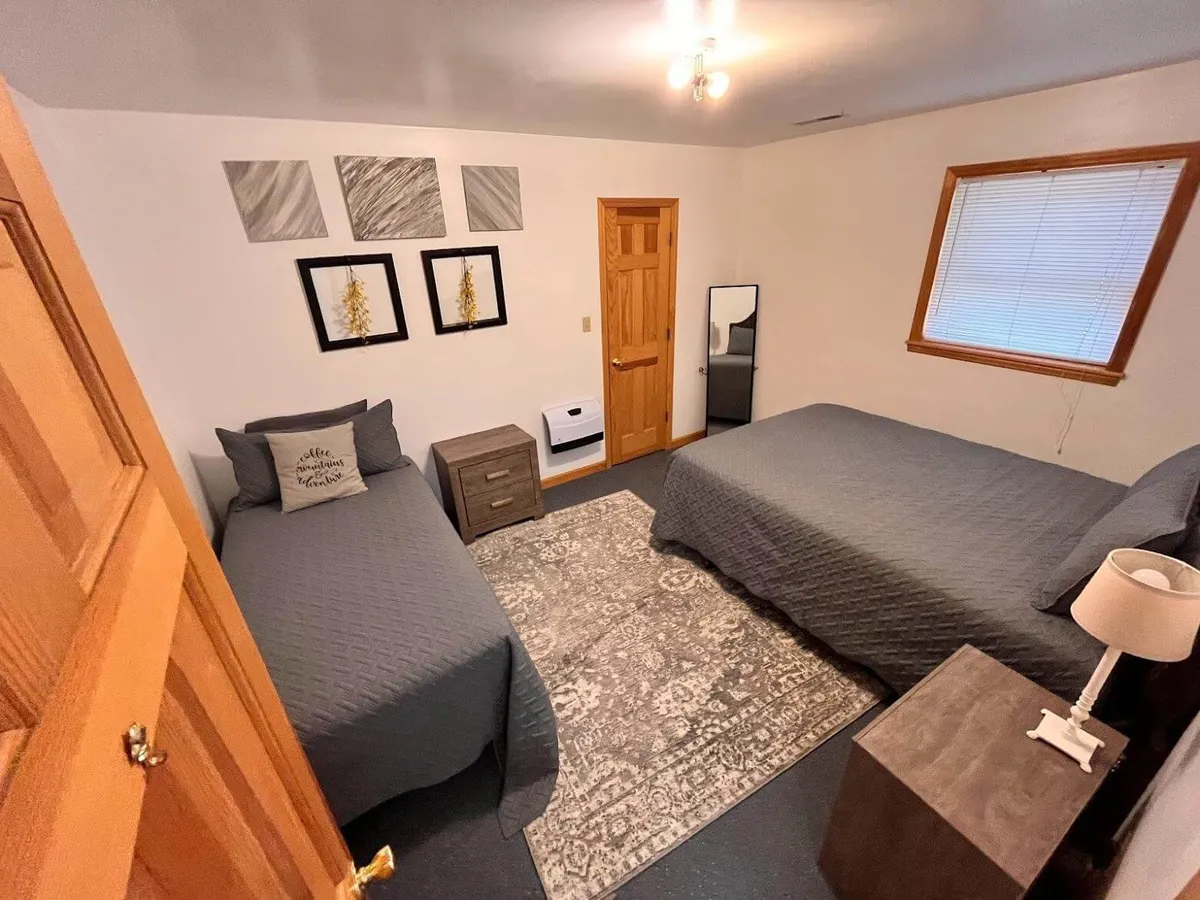A welcoming bedroom featuring two beds, decorative wall art, a nightstand with a lamp, and a mirror. The room is designed for both comfort and flexibility, ideal for accommodating guests of all ages.