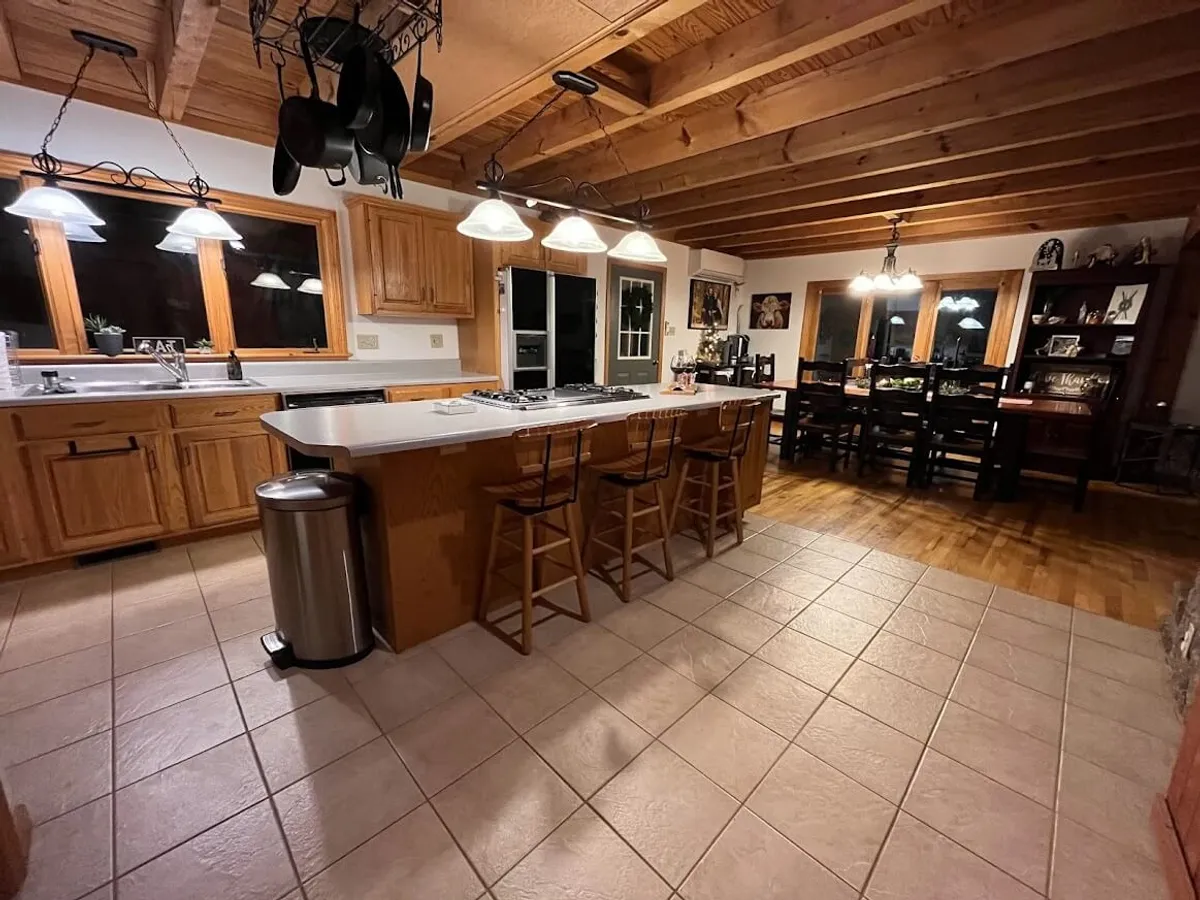 A warm, welcoming kitchen scene featuring a spacious kitchen island, wooden cabinets, and a dining table. The setting emphasizes openness and is alive with the activity of cooking, family gatherings, and casual dining. The layout promotes easy movement and engagement between the kitchen and adjoining spaces, with ample countertops and modern fixtures evident.