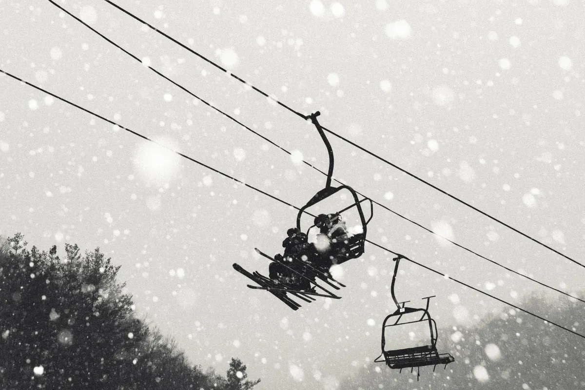 Snowflakes gently fall as a ski lift ascends through tree-lined slopes, capturing the excitement and beauty of winter sports and après-ski moments just outside your door.