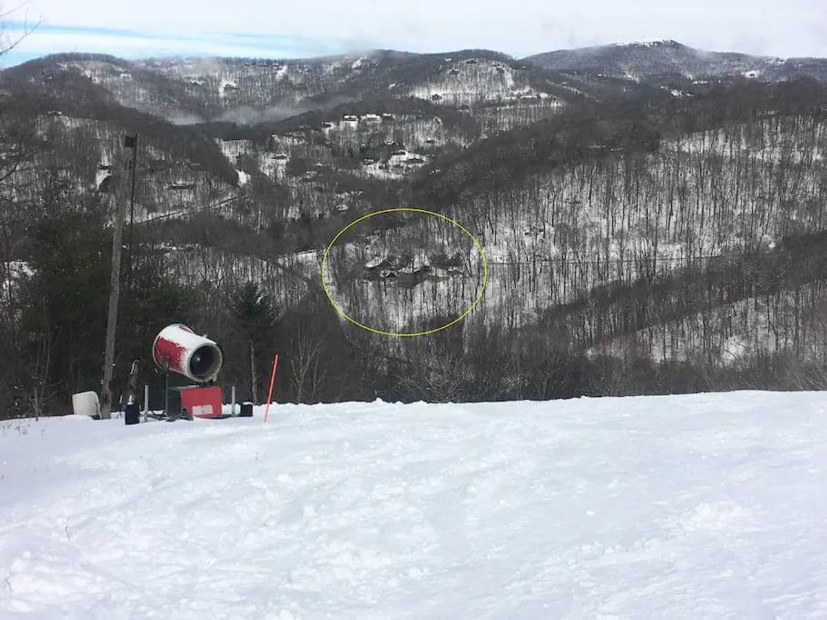 A sweeping view of snow-covered mountains with ski resort buildings in the distance and snow-making equipment in use. The tranquil scene highlights the close proximity to Wolf Ridge Ski Resort and the breathtaking landscape guests can enjoy.