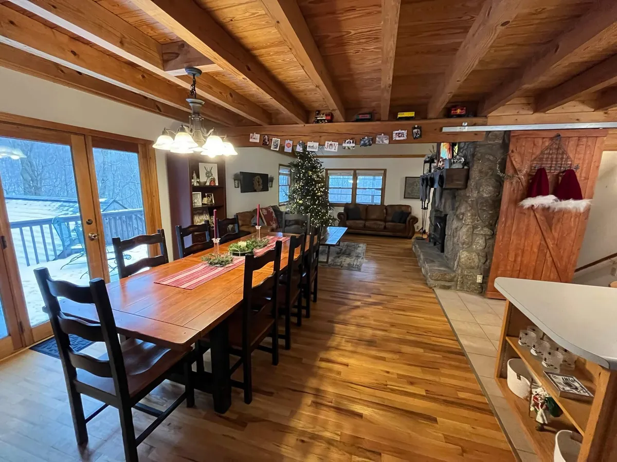 A dining area with a large wooden table set near a stone fireplace, a beautifully decorated Christmas tree, and expansive windows that reveal snow-dusted mountain views. The space is styled with festive, cozy touches for group meals and celebrations.