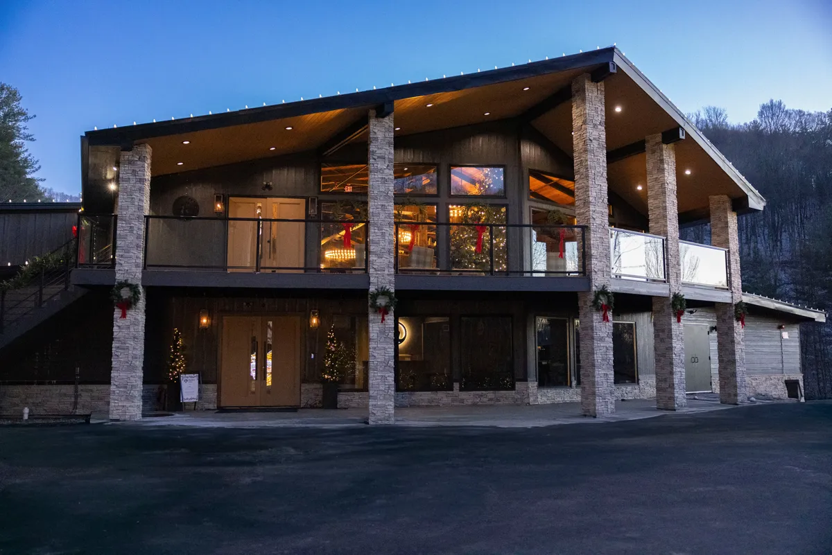 The image captures the welcoming front entrance of the home, highlighted by decorative stone pillars, a balcony with railings, and festive holiday decorations. The scene exudes a sense of arrival and celebration, ideal for families coming together after a day of adventure.