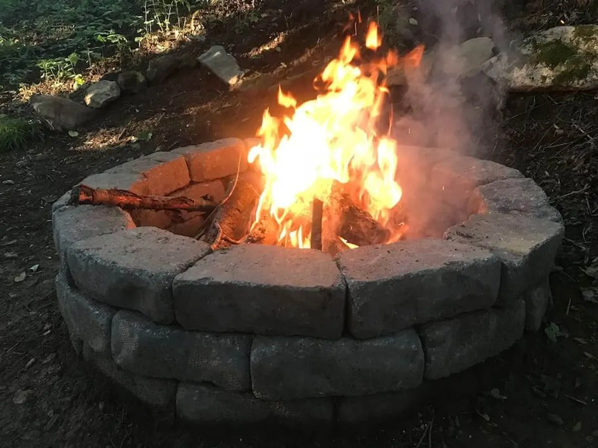 A communal campfire glows in a stone fire pit, surrounded by the natural mountain landscape. Friends and family can gather around for stories, snacks, and unforgettable evenings under the stars.